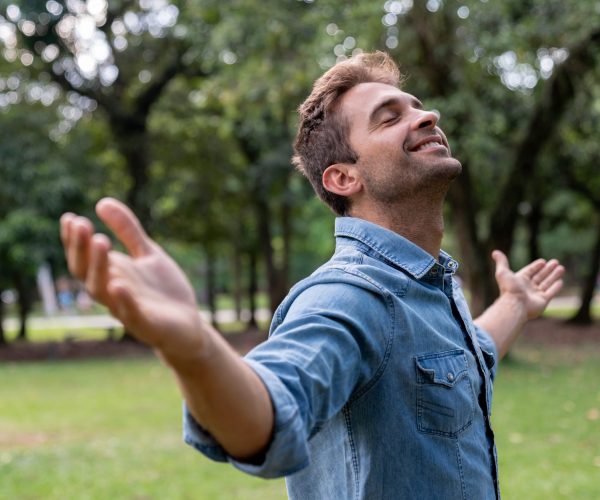 Portrait of a peaceful man relaxing at the park with arms open and smiling - wellness concepts