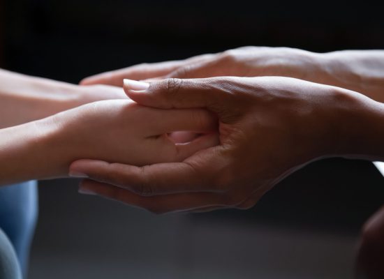 Close up young african american woman holding hand of female caucasian friend, giving psychological help, supporting in difficult life situation. Sincere mixed race people holding trusted conversation